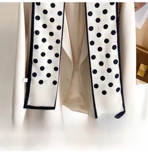 Close-up of a white polka dot skinny scarf tied on a beige double-breasted blazer lapel