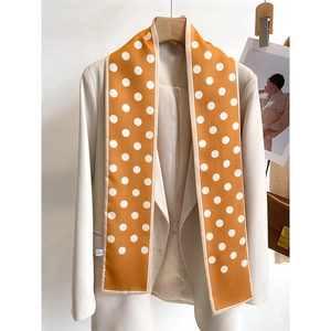 Close-up of bright orange polka dot skinny silk scarf styled with a beige blazer