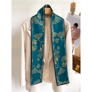 Narrow silk scarf with golden ginkgo leaves on dark green, styled on a beige blazer