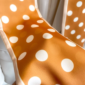 Close-up of orange polka dot silk scarf showing smooth texture and detailed stitching