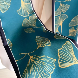 Detailed close-up of dark teal silk scarf featuring gold ginkgo leaf prints and contrast edges