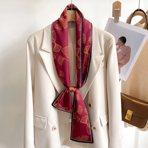 Elegant red skinny scarf with golden ginkgo leaves styled on a white blazer