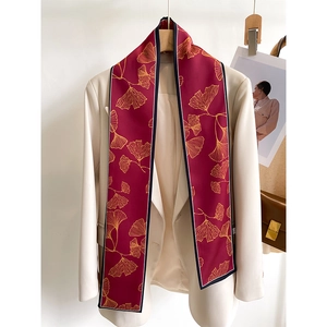 Detail of burgundy silk twilly scarf with gold ginkgo leaf pattern on white blazer