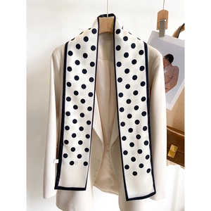 Close-up of a long silk scarf with black polka dots styled on a beige blazer jacket