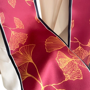 Detail of burgundy silk scarf with golden ginkgo leaves and striped border texture