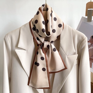 Close-up of a beige polka dot silk scarf tied on a cream blazer with satin finish