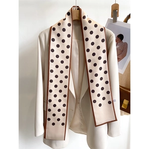 Close-up of narrow polka dot silk scarf draped over a beige blazer with a brown bag