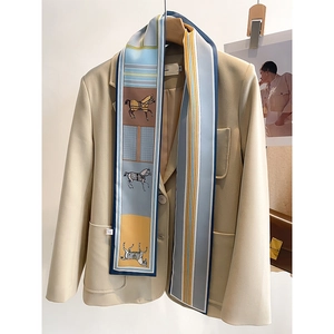 Detail of equestrian print silk twilly scarf styled on a beige suit blazer