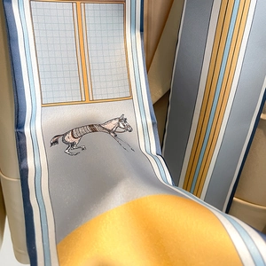Close-up of a long silk scarf with horse patterns and gold accents on a leather background