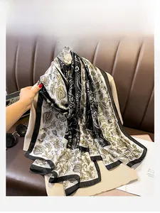 Detail of silk-like scarf with black and gold paisley patterns draped on beige clothing