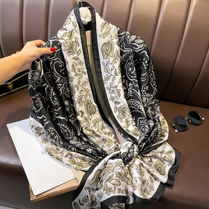 Elegant silk scarf with black white and gold paisley floral patterns on leather couch