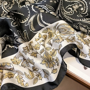Macro detail of silk scarf with black paisley and golden floral patterns on draped fabric