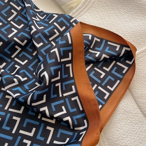 Macro shot of geometric letter print silk scarf with caramel contrast border texture