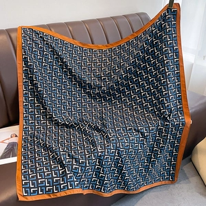 Detail of silk square scarf hanging on a leather sofa with navy geometric L-patterning