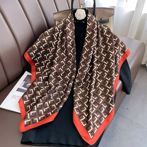 Detail of geometric pattern silk scarf in brown and black with bold red hem edges