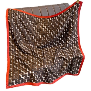 Red and brown geometric pattern square silk scarf displayed on a leather surface