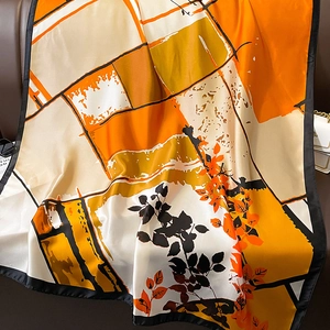 Close-up of silk-like scarf with orange floral pattern draped on a leather sofa
