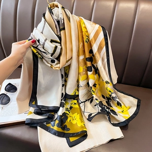 Elegant floral silk scarf with yellow and black leaf patterns on a luxury sofa setting