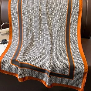 Long silk-like scarf with orange and grey geometric print draped on a leather chair