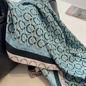 Dettaglio di sciarpa di seta azzurra con motivo a catena drappeggiata su borsa in pelle