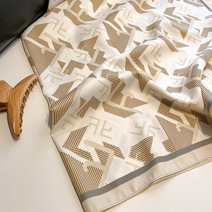 Detail shot of silk scarf fabric showing smooth twill texture and monogram pattern
