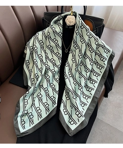 Détail d'un foulard soyeux vert menthe avec motif monogramme et bordure noire