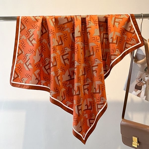 Detail of a bright orange silk scarf with letter print and twill texture on a rack