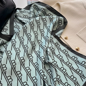 Détail d'un foulard en soie vert menthe avec motif monogramme et finition satinée