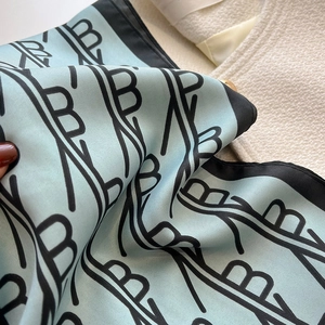 Détail macro du foulard en soie montrant la texture satinée et le motif de lettres