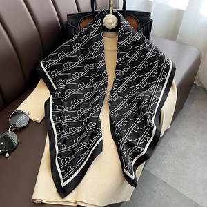 Détail d'un élégant foulard en soie à motifs noir et blanc drapé sur un pull beige