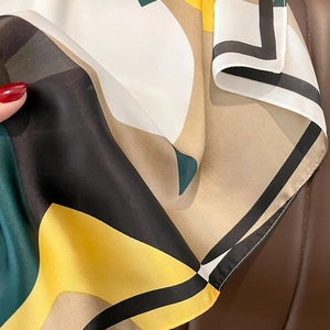 Macro view of geometric color-block silk scarf with yellow, green, and khaki patterns