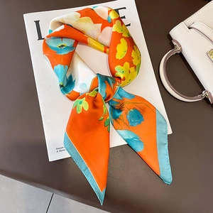 Carré de soie orange vif avec motifs floraux bleus posé sur un magazine de mode