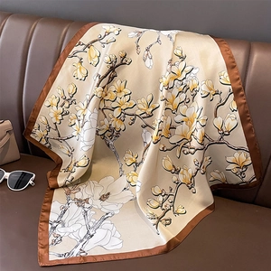 Eleganter Seidenschal mit Magnolien-Print in Apricot und dunkelbraunem Rand auf Lederhintergrund