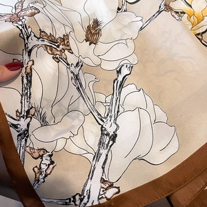 Detail eines Seidenschals mit Magnolienprint und kaffeebraunen Steppkanten