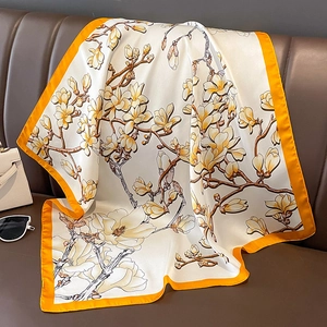 Detail eines Seidenschals mit Magnolienmuster auf Lederhintergrund mit Accessoires
