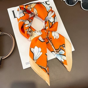 Orangefarbenes Seidentuch mit weißen Magnolienblüten auf dunklem Lederhintergrund