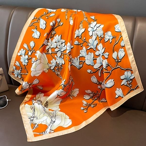 Detailaufnahme von orangefarbenem Seidenschal mit weißem Magnolienmuster und Satinkante