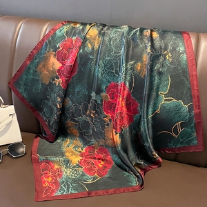 Peony floral print satin square scarf in dark green and red draped on a leather sofa