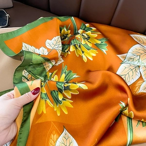 Detailed view of silk-like satin square scarf with orange sunflower prints and green edges