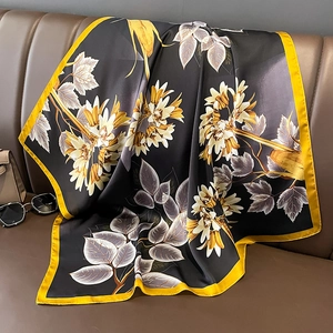 Elegant black silk-like square scarf featuring yellow floral patterns on a leather sofa