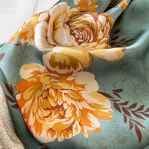 Détail de l'écharpe en soie verte avec imprimés de roses orange et texture satinée douce