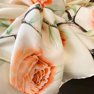 Macro view of printed silk scarf showing orange rose patterns and glossy satin texture