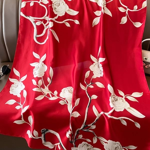 Detailed texture of red floral silk scarf draped with sunglasses and stylish handbag