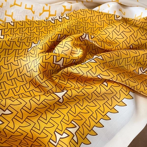 Gros plan d'un foulard en soie à motif géométrique jaune moutarde et crème élégant