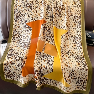 Fashionable large leopard print silk scarf with H pattern on a leather sofa