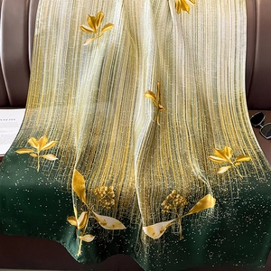 Élégante écharpe en soie dégradé vert avec imprimés dorés drapée sur un canapé en cuir