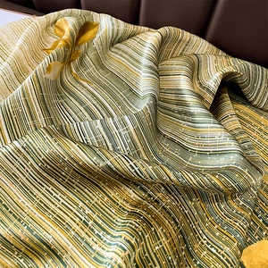 Détail macro d'un foulard de plage soyeux avec rayures vertes et motifs floraux dorés