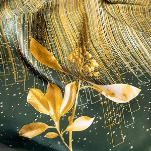 Détail d'une écharpe en soie montrant un tissu vert foncé brillant aux motifs dorés