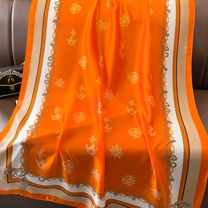 Orange nautical silk scarf with anchor chain patterns and tassels on a leather sofa