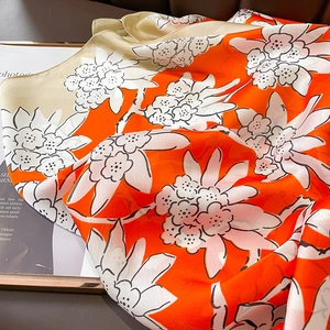 Detailed view of floral silk scarf featuring bright orange and cream artistic patterns
